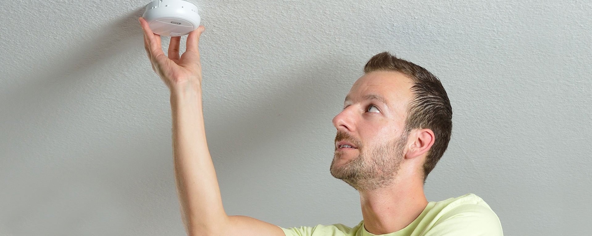 Ein Mann befestigt einen Rauchmelder an der Decke