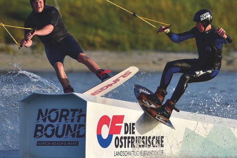 Zwei Personen fahren Wasserski über eine Rampe mit dem OF Logo